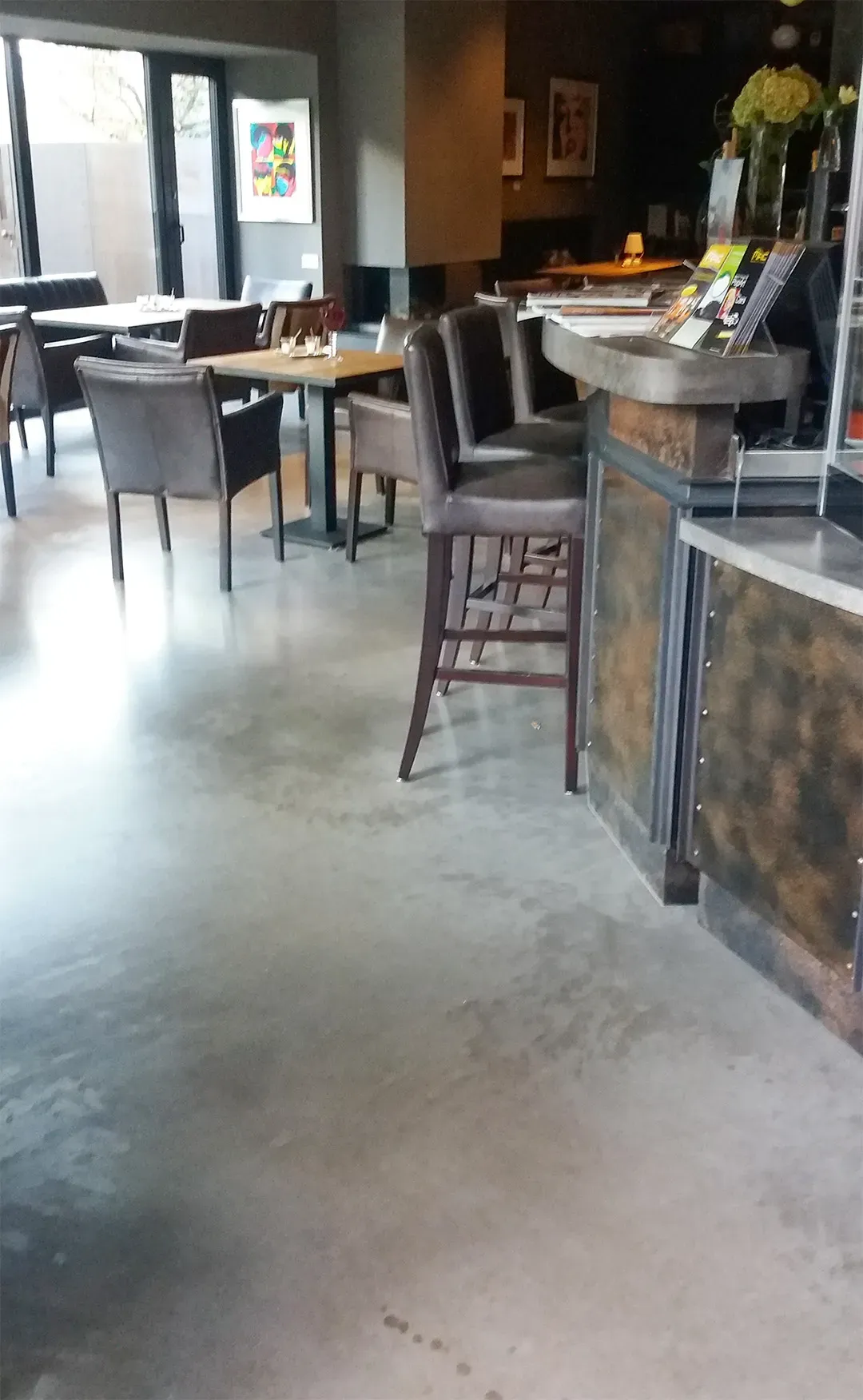 Gastrobereich mit grauem Betonboden, modernen Möbeln und einem einladenden Tresen