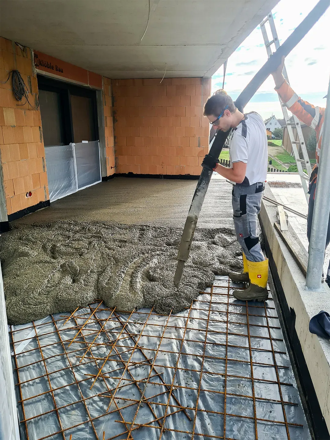 Balkonbau mit Betonierung auf Bewehrungsmatte, ein Arbeiter mit Gummistiefeln führt den Betonschlauch