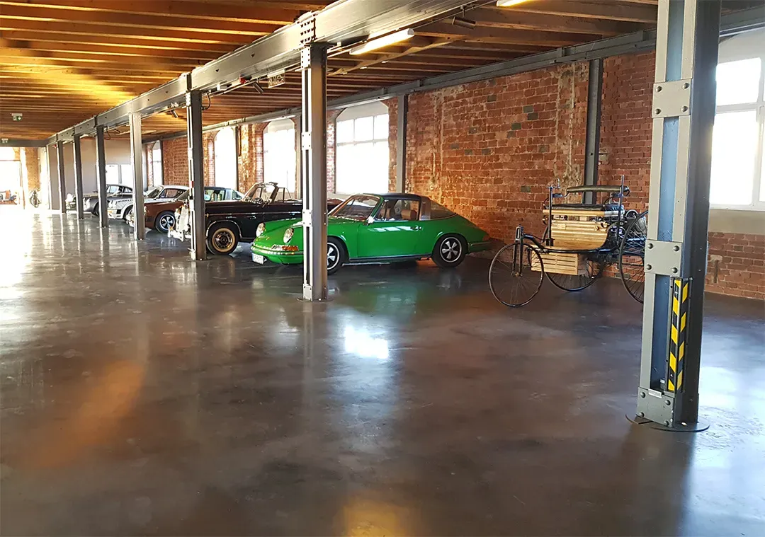 Großer Raum mit poliertem Betonboden, Backsteinwänden, Autos und einer historisch anmutenden Fahrmaschine