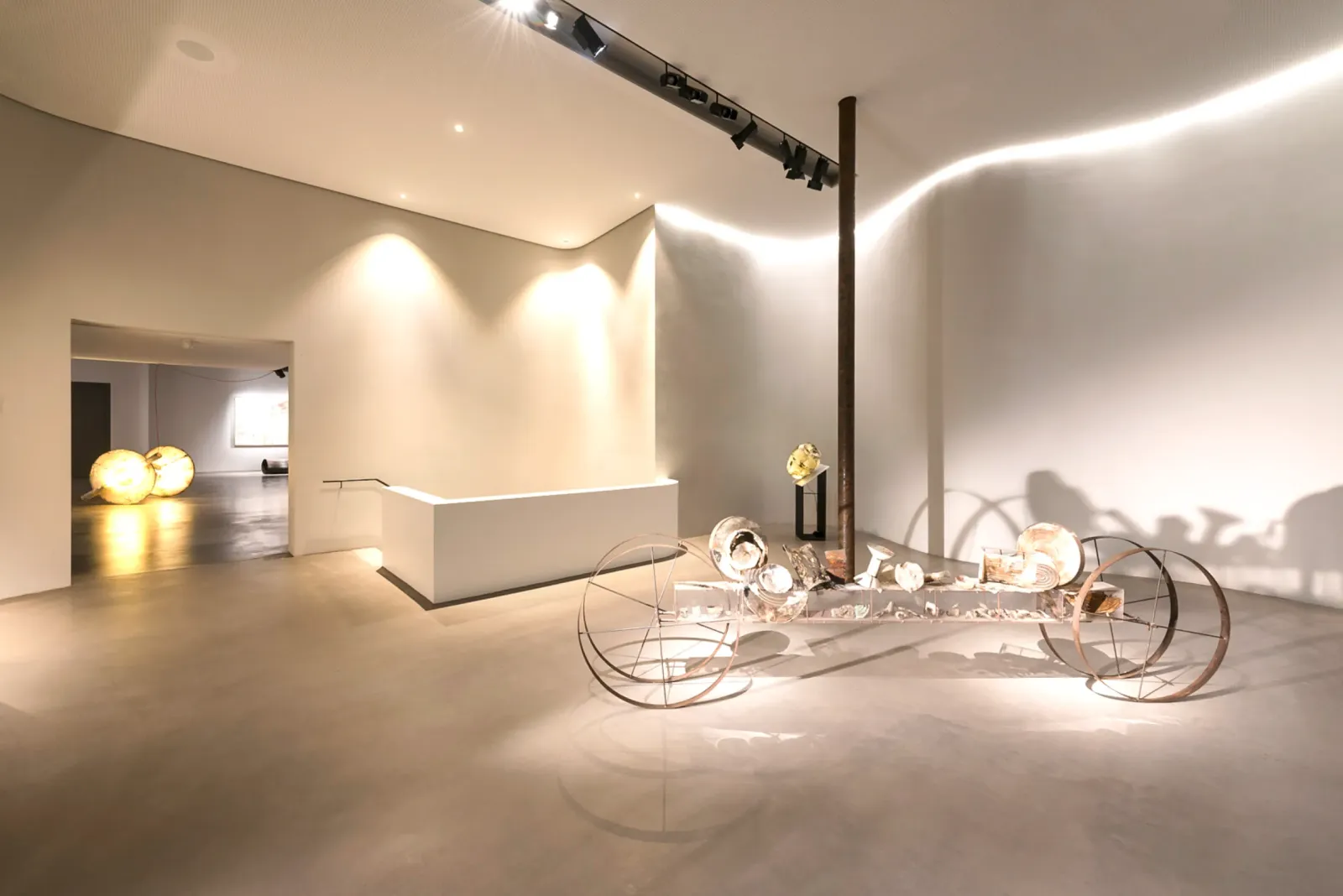 kunstvoll gestaltete Ausstellung mit skulpturalen Elementen und stimmungsvoller Beleuchtung in einem offenen Galerieraum