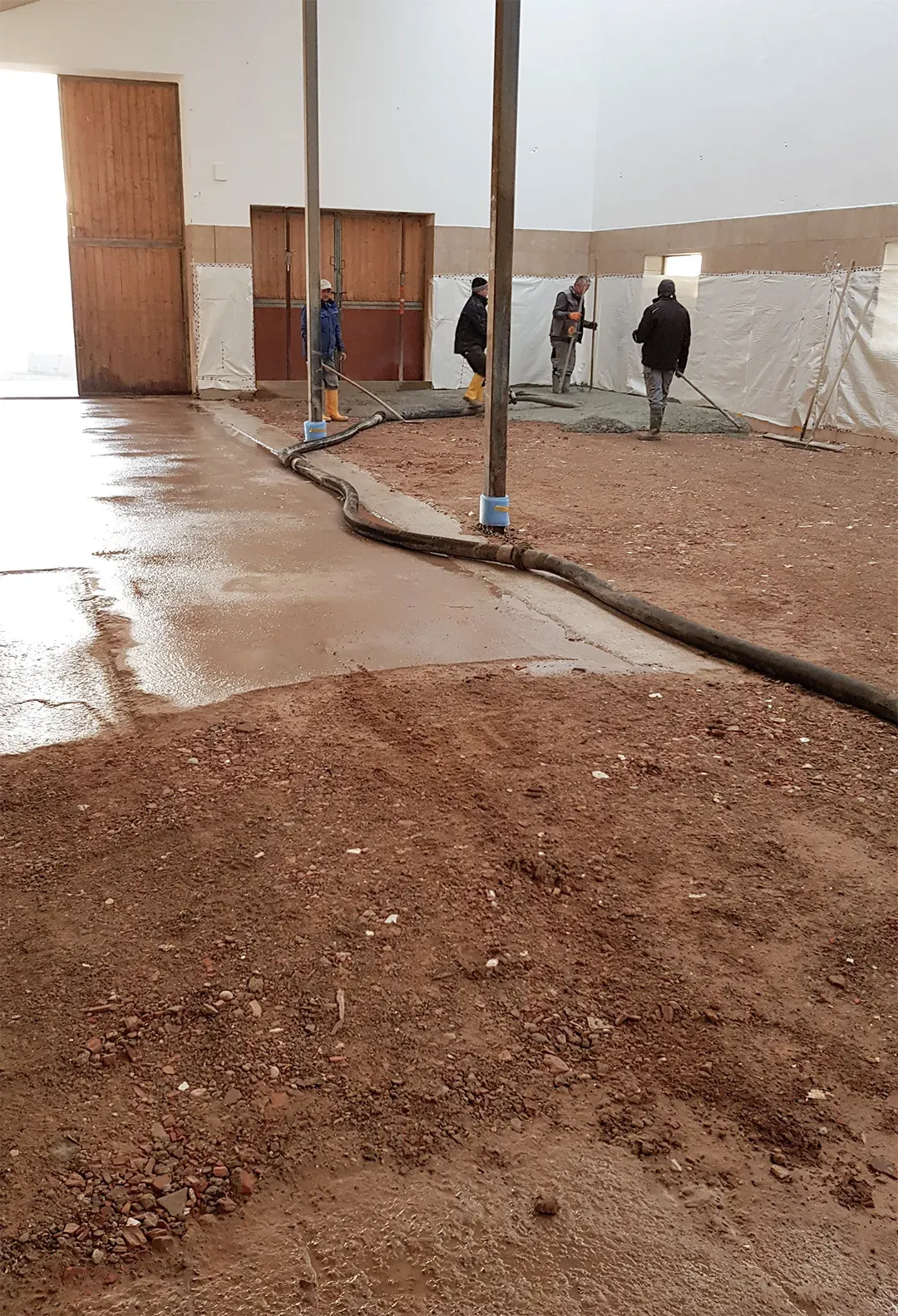 Arbeiter führen Betonierarbeiten in einer großen Halle mit Erduntergrund durch