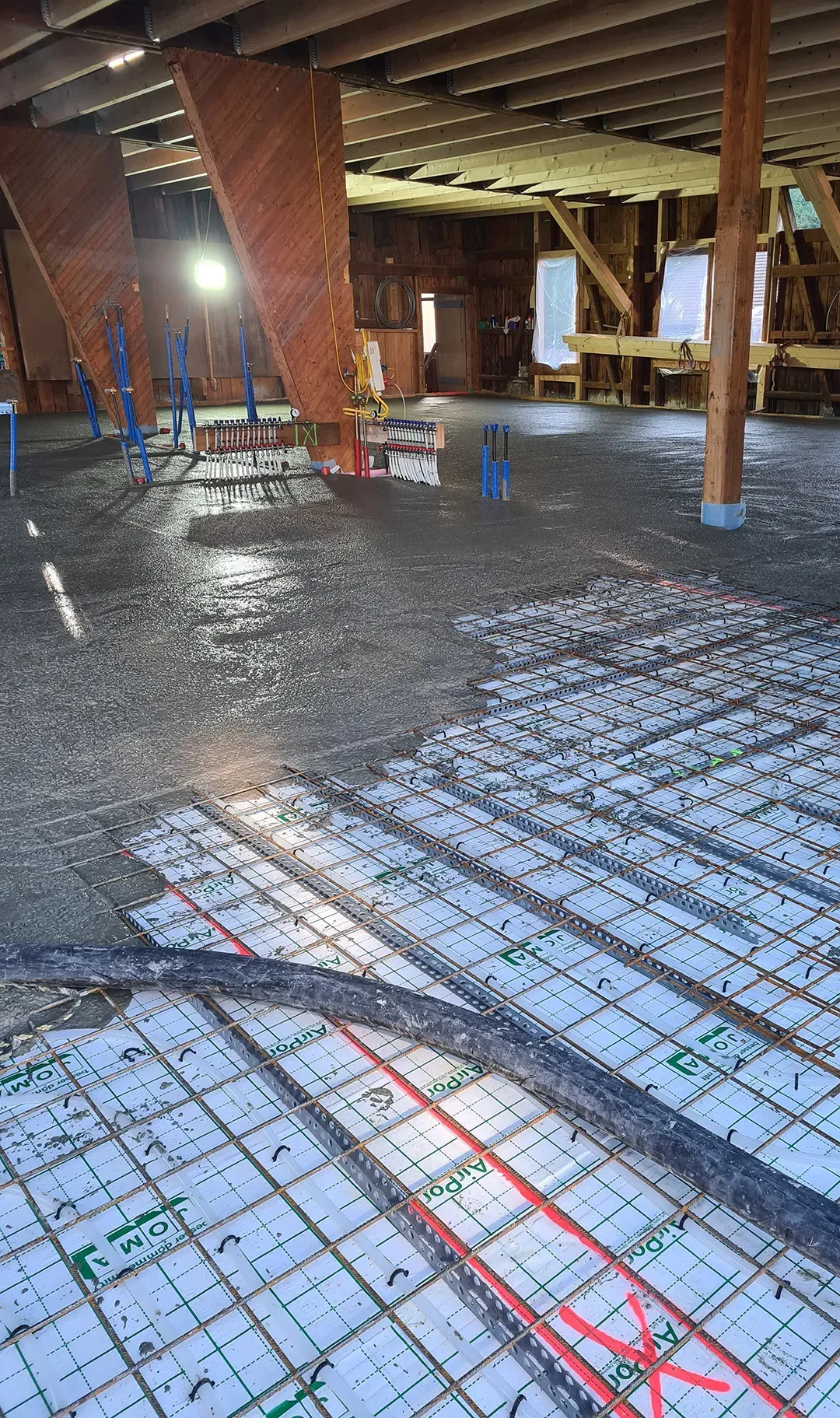 Ein großer Raum mit Rohbaucharakter, frisch gegossener Estrich und einer Fußbodenheizung mit sichtbaren Verteilerrohren und Installationen