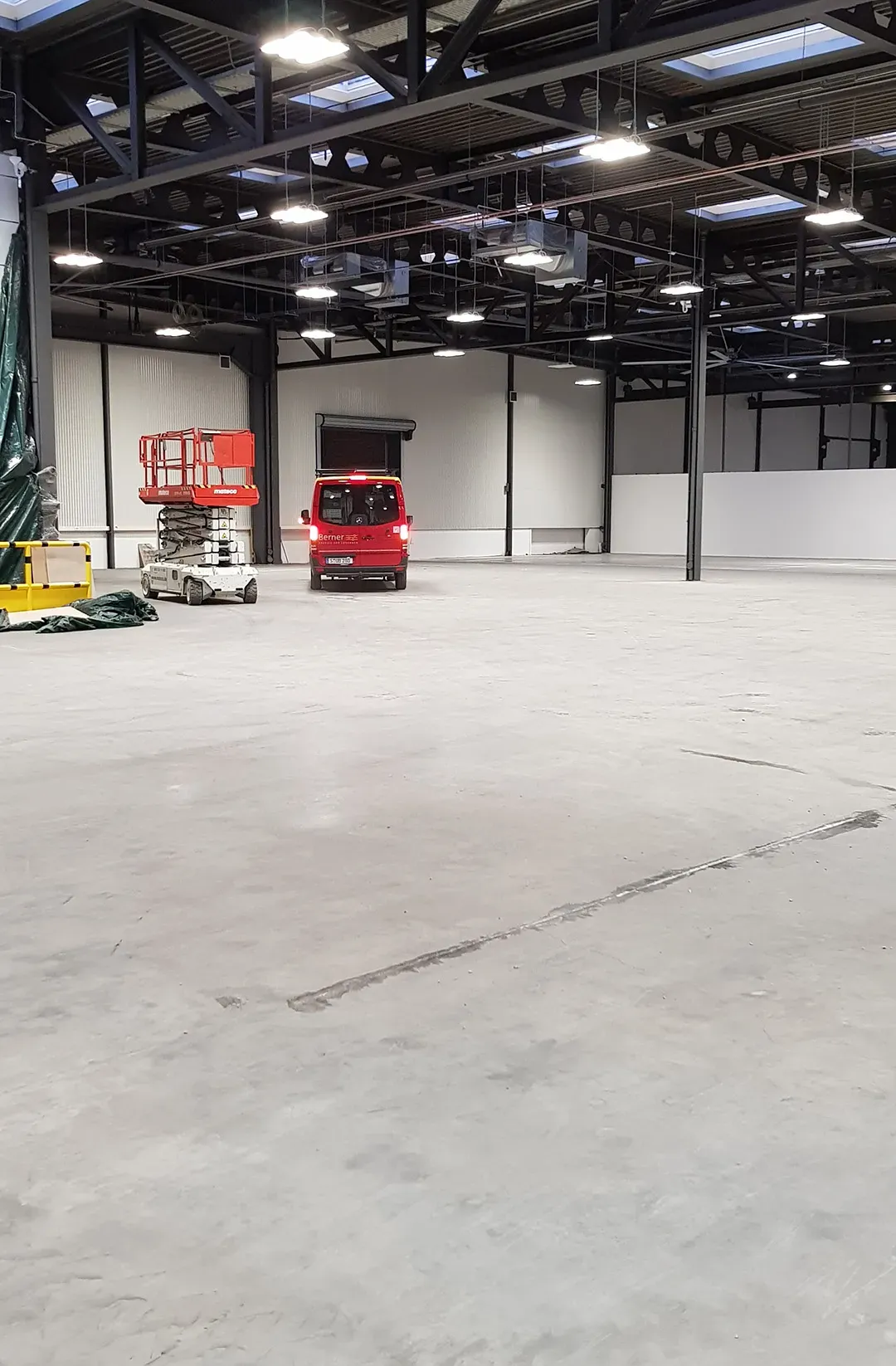 Große Industriehalle mit montierten Lichtern, einem Kleintransporter und Hebebühnen