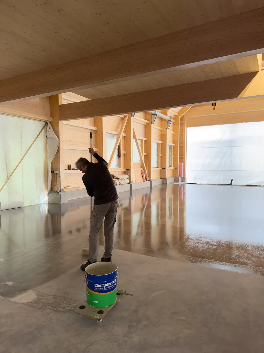 Arbeiter trägt Bodenversiegelung auf polierten Betonboden in einer modernen Halle auf