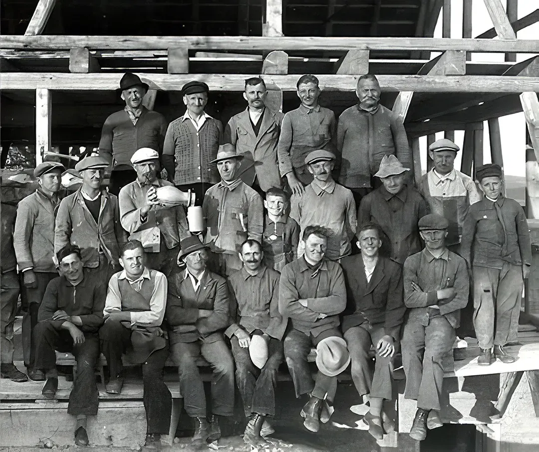 Gruppe von Arbeitern in traditioneller Arbeitskleidung vor einer Holzgerüstkonstruktion
