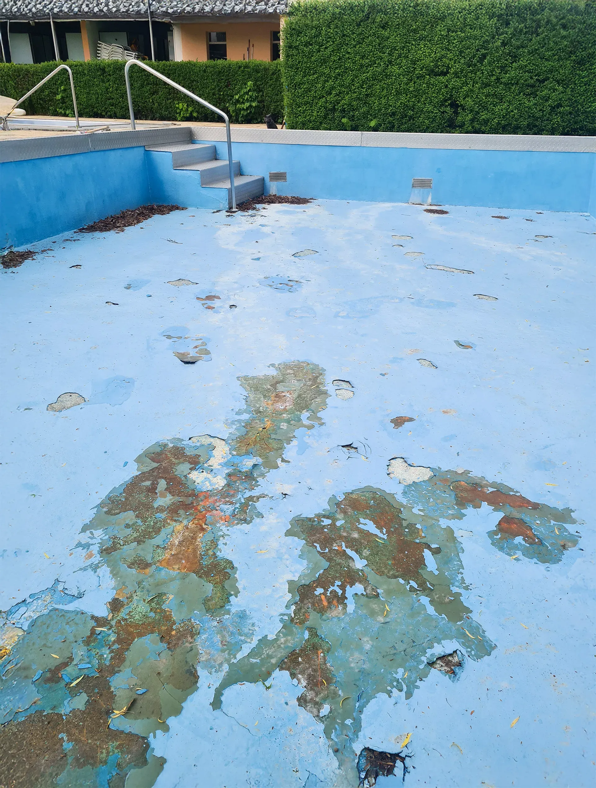 Schwimmbecken mit abgenutztem blauen Untergrund und sichtbaren Farbschäden