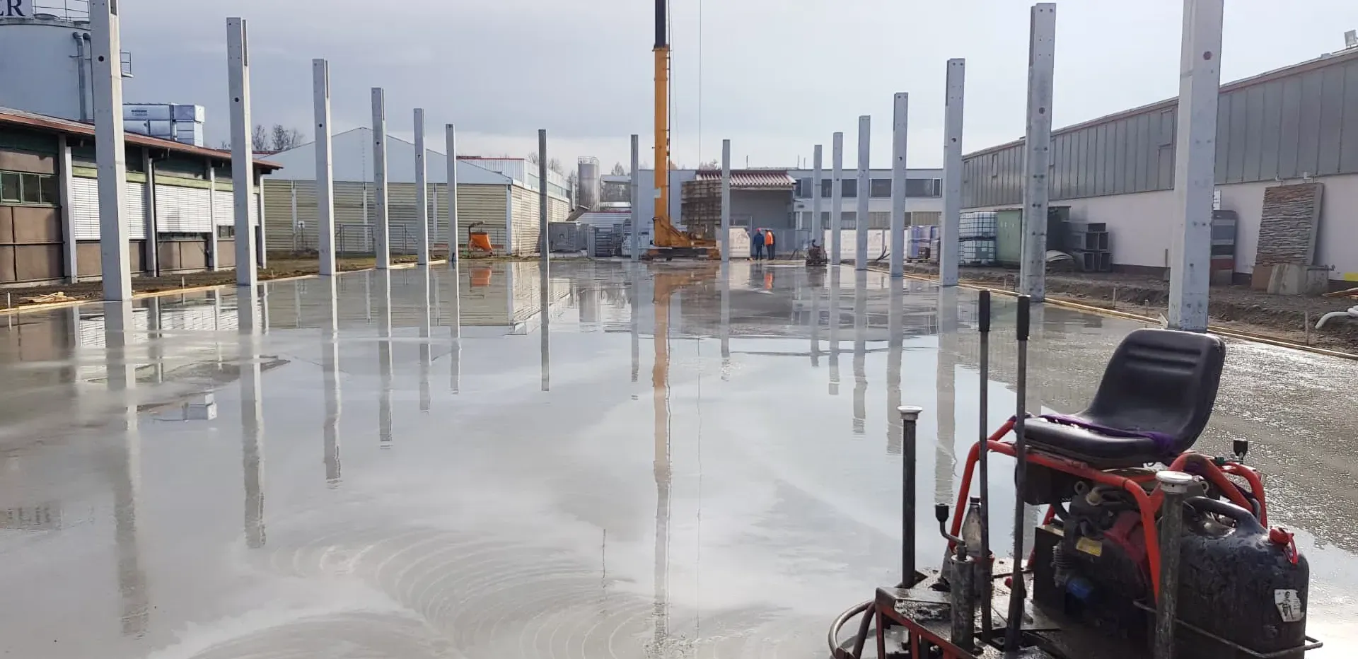 Baustelle mit noch nassem Betonboden und vertikalen Stahlträgern in der Aufbauphase