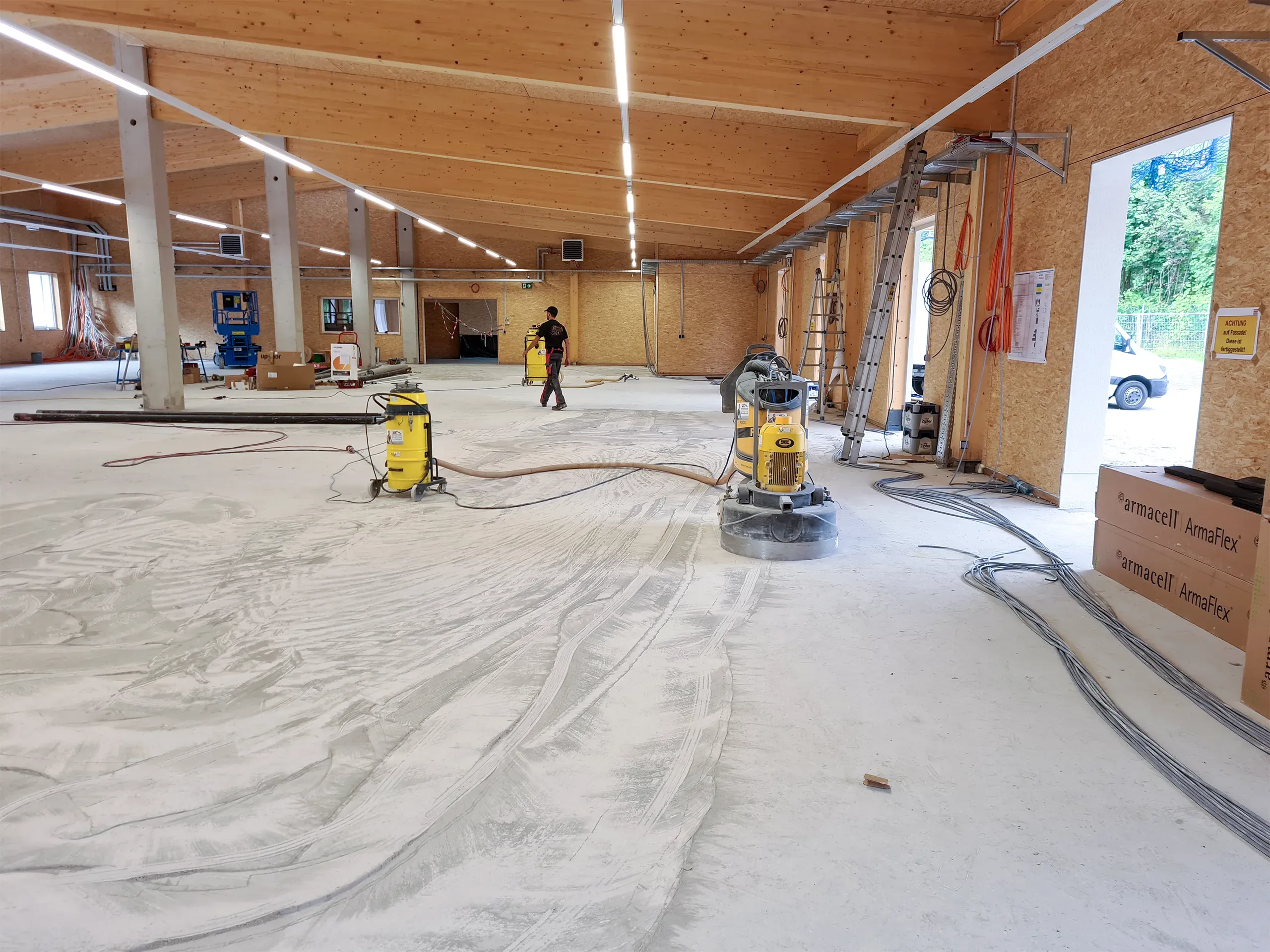 Bauhalle mit Betonboden während der Bearbeitung und Schleifmaschinen im Einsatz