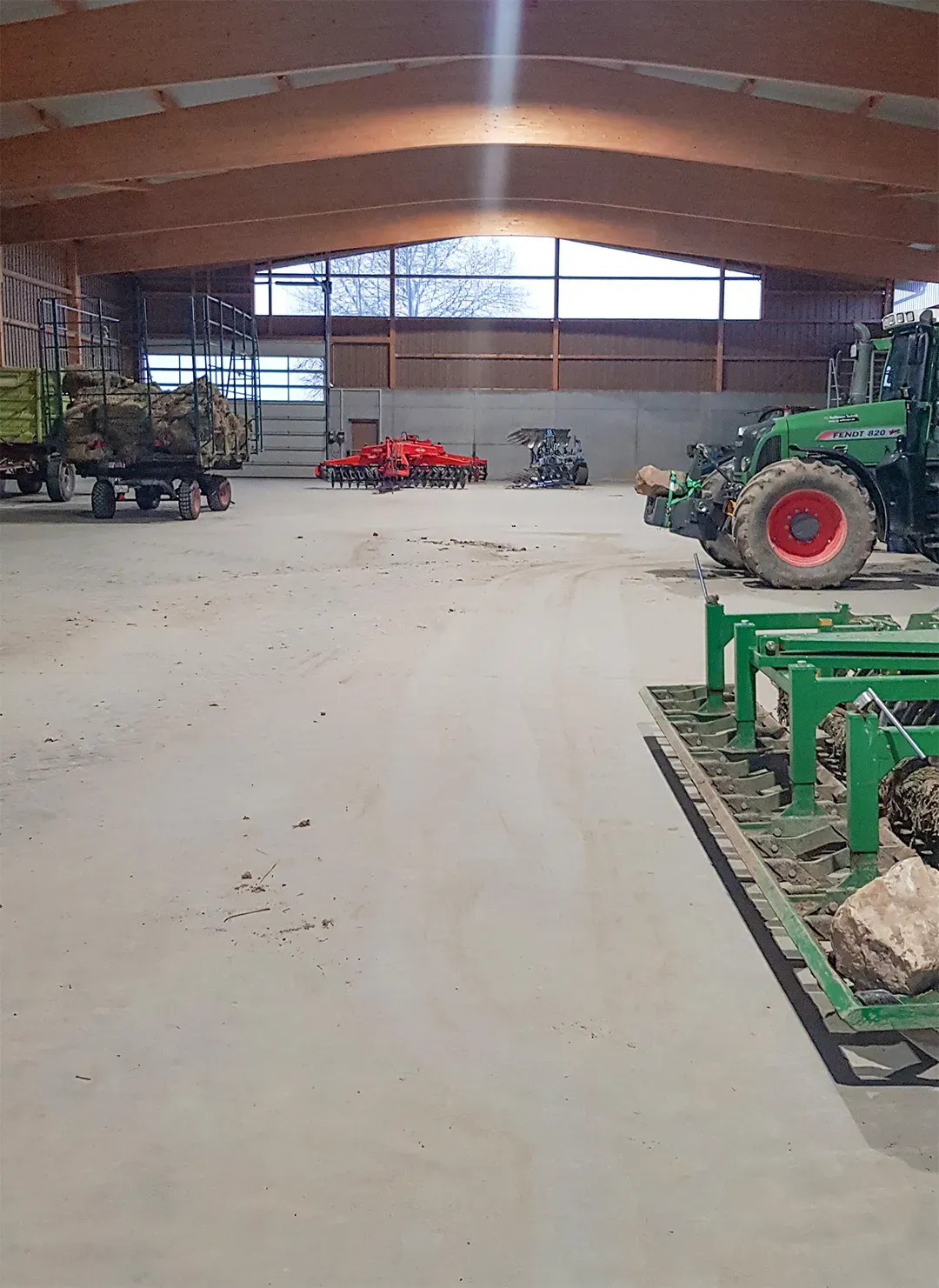 landwirtschaftliche Halle mit Traktoren, Anhängern und Arbeitsgeräten auf freier Betonfläche