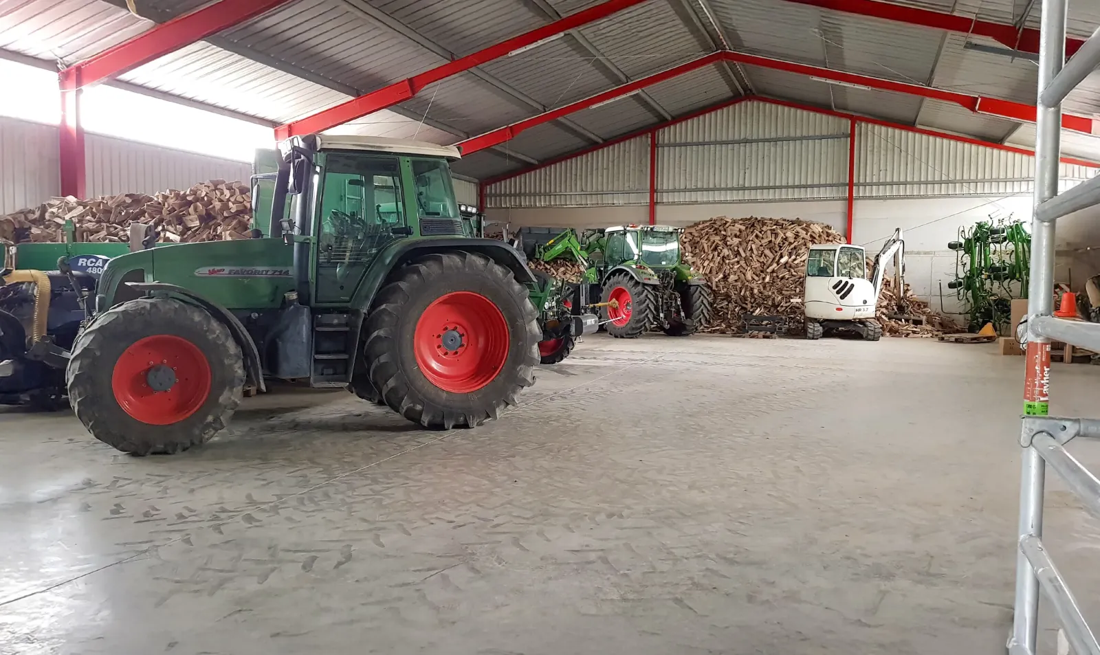 Innenraum einer Lagerhalle mit Traktoren, Holzhaufen und landwirtschaftlichen Maschinen