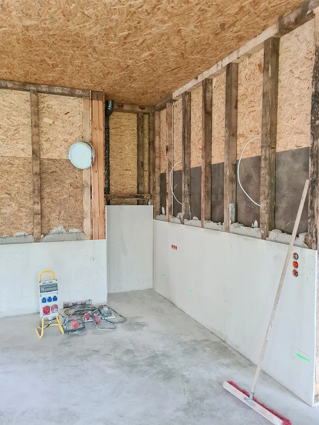 Rohbau eines Raumes mit OSB-Platten an den Wänden, sichtbarer Wanddämmung, Werkzeugen und Besen auf dem Boden