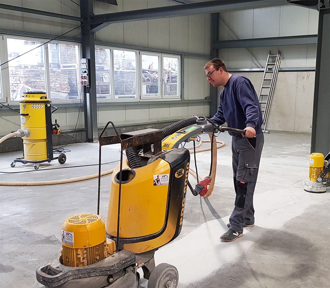 Werkshalle mit Bodenbearbeitungsmaschine für Schleifarbeiten und weiteren Reinigungsgeräten im Hintergrund