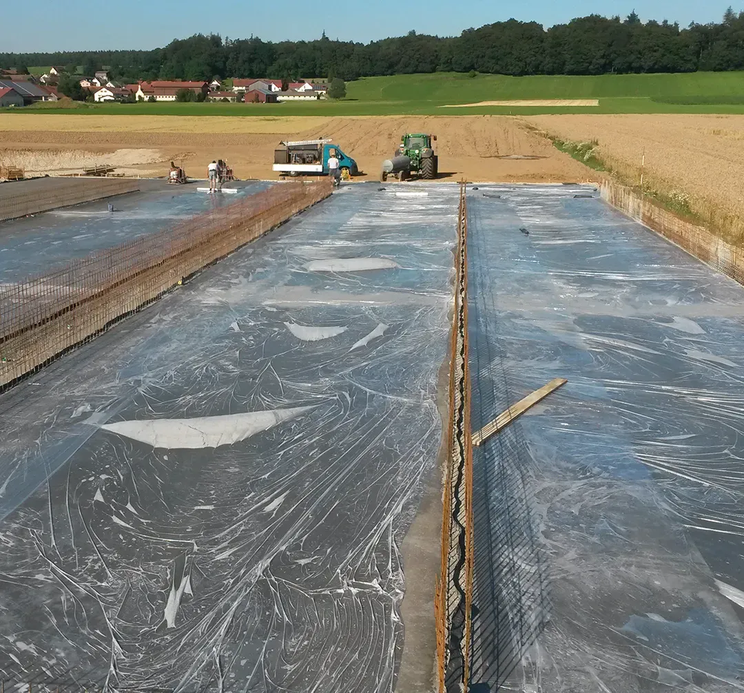 großflächige Betonplatte mit Folie abgedeckt und landwirtschaftlicher Umgebung