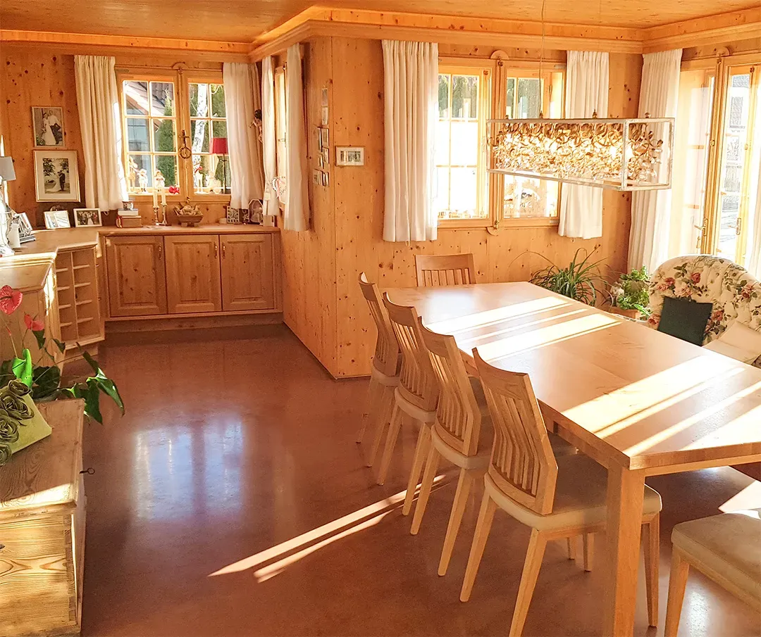 Heller Wohnraum mit Holzwänden, einem großen Esstisch und dekorativen Pflanzenarrangements