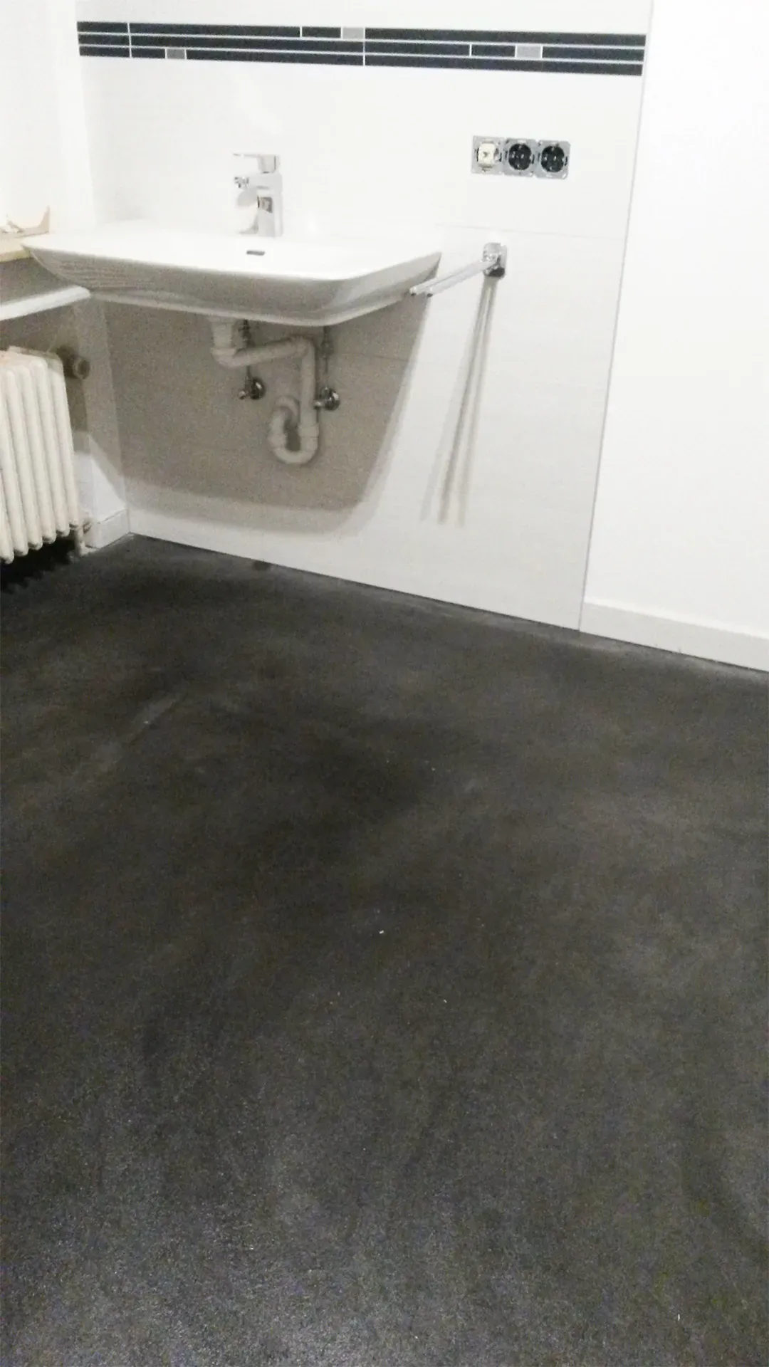 Badezimmer mit schlichtem weißen Waschbecken, schwarzen Fliesenboden und minimalistischer Wandgestaltung