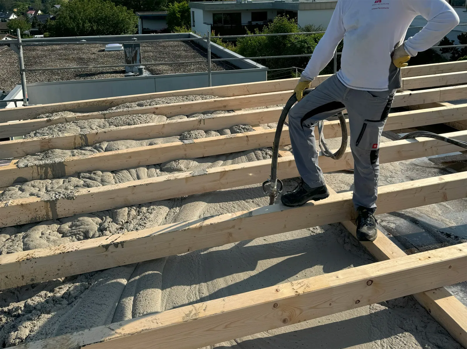 Arbeiter verteilt Dämmmaterial auf einem Dachboden mit sichtbaren Holzbalken und eingebrachten Dämmstoffbahnen