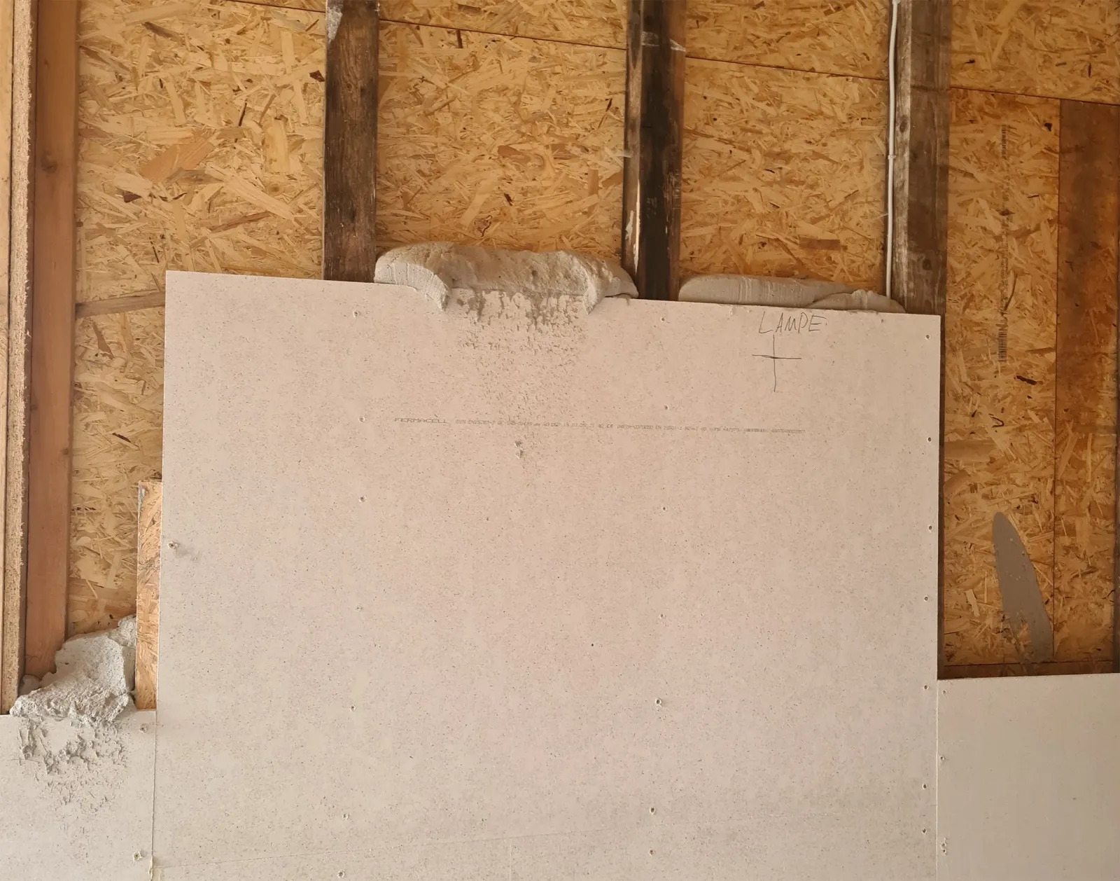 Holzkonstruktion mit einer Wand aus teils verkleideten OSB-Platten und eingetragener Dämmmasse
